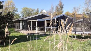 Ein modernes Haus mit überdachter Terrasse, umzäunter Garten und hohem Gras.
