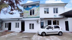 A two-story building with a white exterior, a car parked in front, and a mural on the upper wall. - Hostel Karadeniz ok (Tashkent)