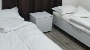 A bedroom with two single beds, a small white dresser, and a dark curtain. - Hostel Karadeniz ok (Tashkent)
