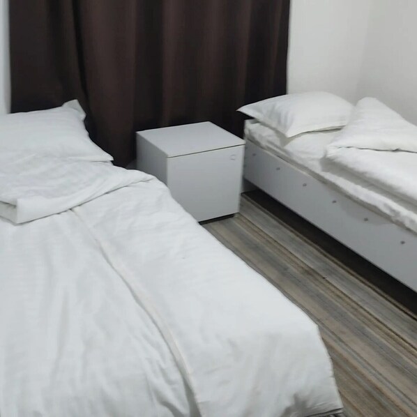 A bedroom with two single beds, a small white dresser, and a dark curtain. - Hostel Karadeniz ok (Tashkent)