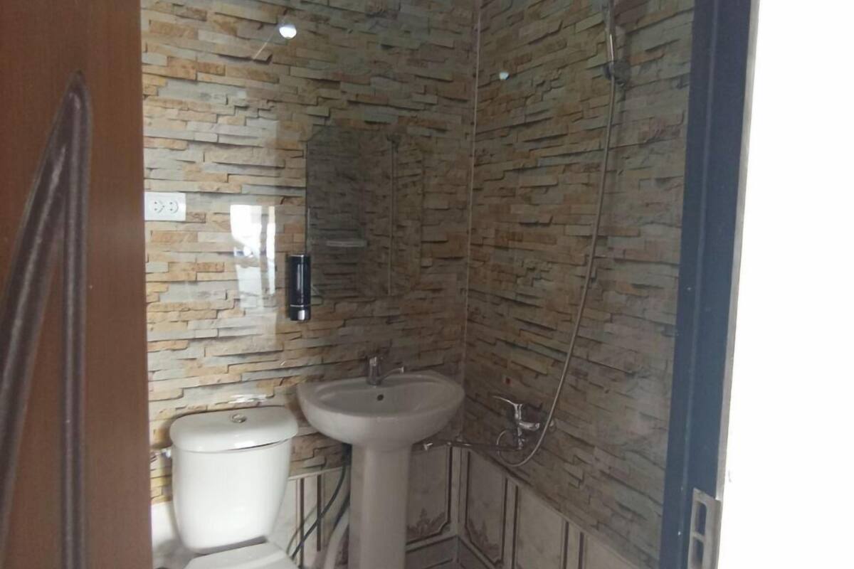 Une petite salle de bain comprenant des toilettes, un lavabo et une douche. Les murs sont recouverts d’un motif qui imite la pierre.