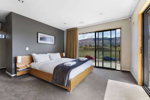 A modern bedroom with a large bed, a nightstand, a window with a view of mountains, and a sliding glass door.
