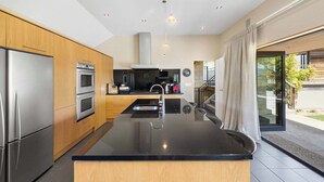 Een moderne keuken met een centraal eiland, roestvrijstalen apparatuur en uitzicht op de buitenruimte.