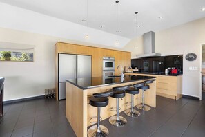 A modern kitchen with a central island, bar stools, stainless steel appliances, and a clock on the wall.