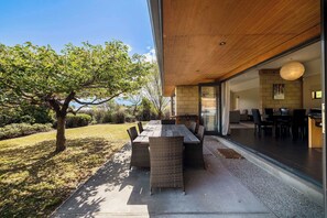 Ein moderner Essbereich im Freien mit Tisch, Stühlen, einem Baum und Blick ins Haus.