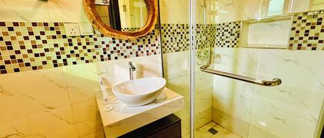 Une salle de bain dotée d’une douche à parois de verre, d’un lavabo blanc avec un plan de toilette en marbre et d’un mur recouvert de mosaïques.