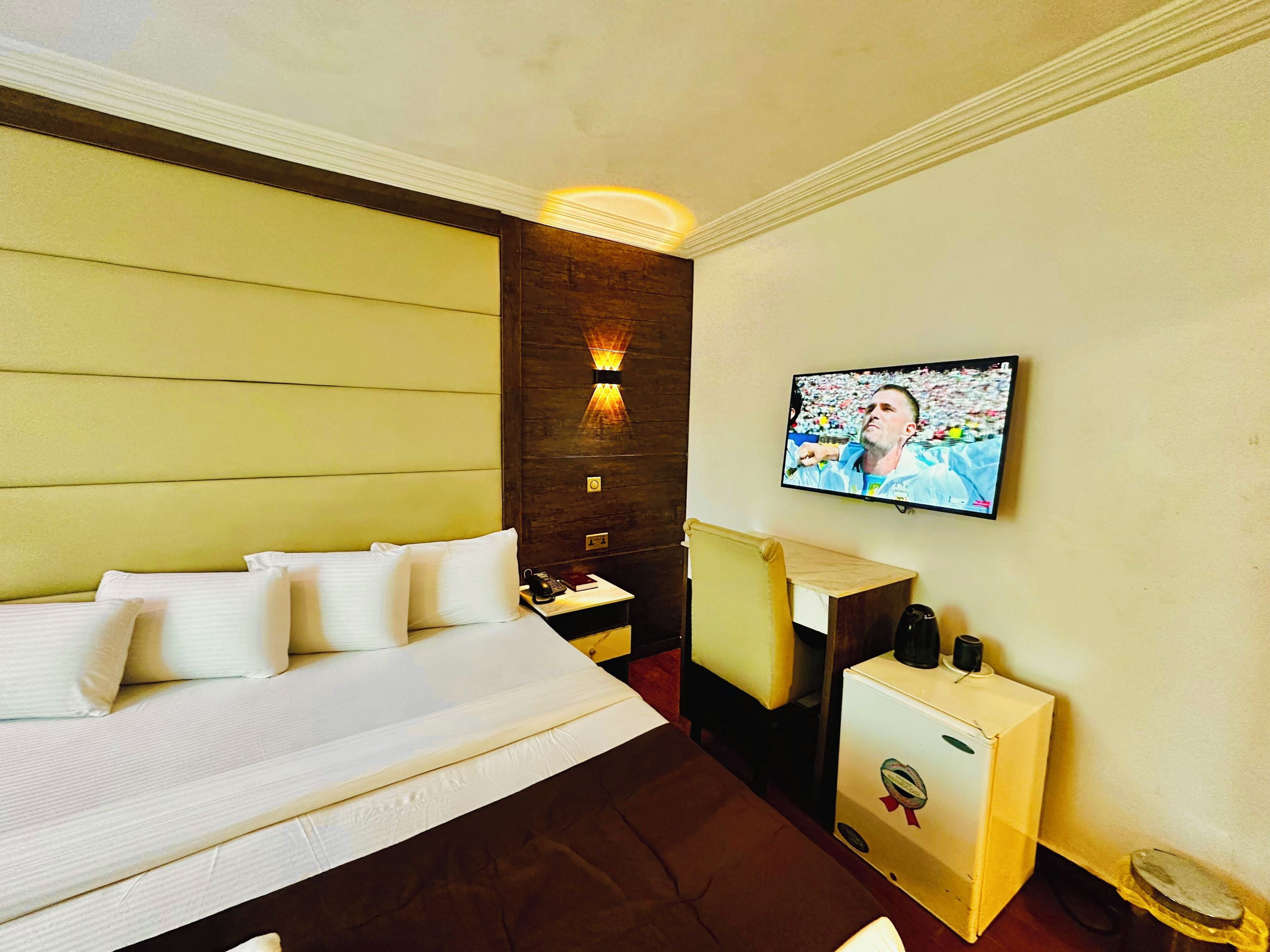 A hotel room with a bed, a desk, a television, and a minibar.