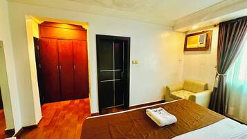 A hotel room with a bed, a chair, a wardrobe, and a door.