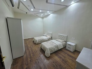 Camera da letto con due letti, pavimento in legno, armadio bianco e soffitto con illuminazione a incasso.