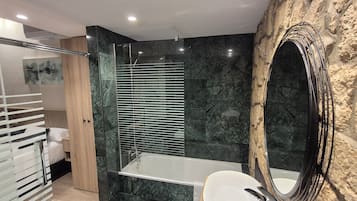 A modern bathroom with a glass-enclosed shower, a large mirror, and a marble wall.
