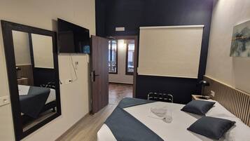 A hotel room with a bed, a desk, a chair, a mirror, a wardrobe, and a view of the outside.