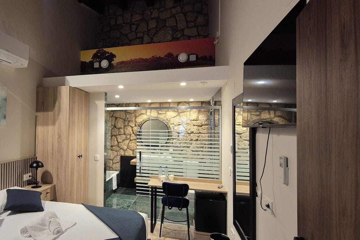 A modern hotel room with a bed, a desk, and a stone wall.