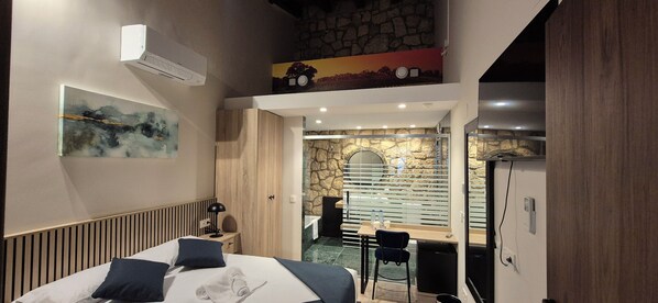 A modern hotel room with a bed, a desk, and a stone wall. - Vineam Hotel (La Muela)