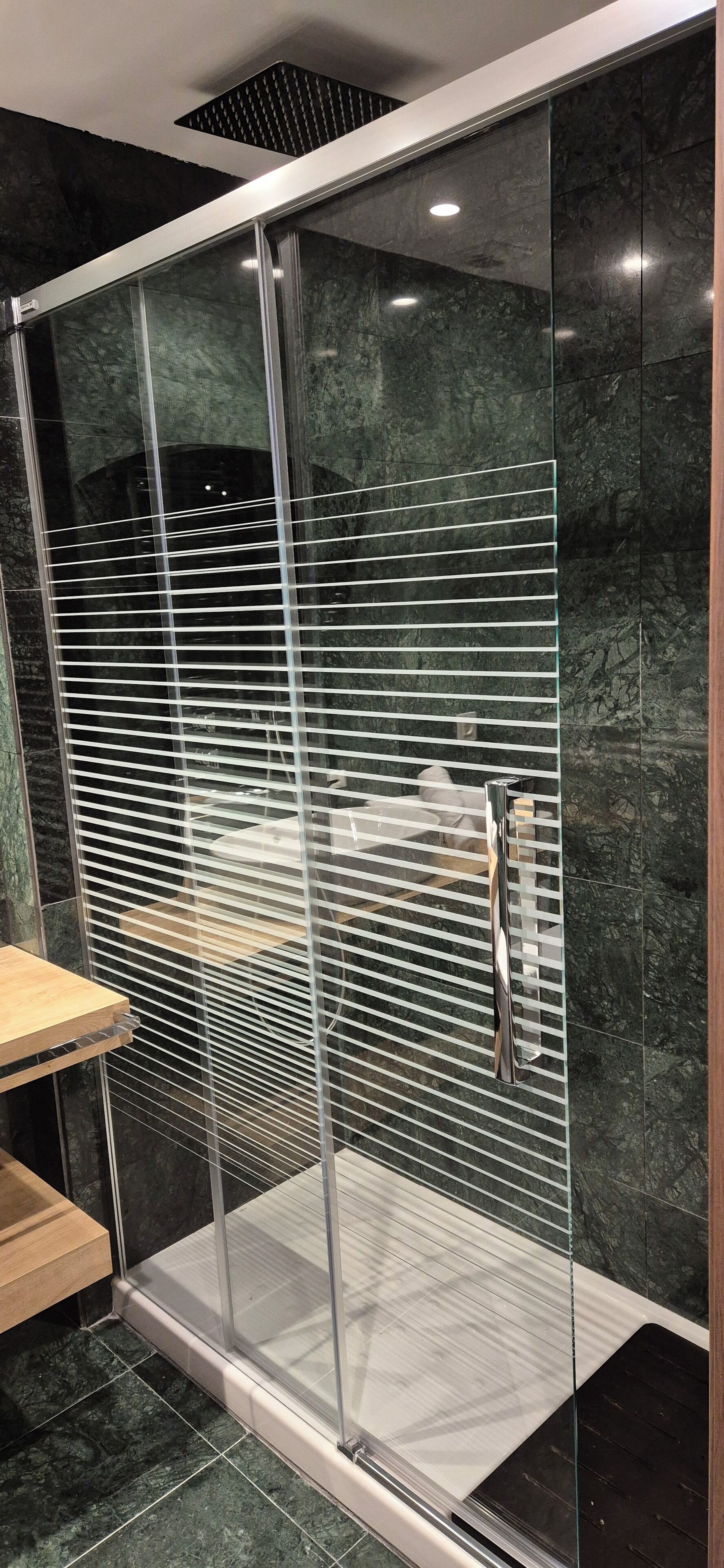 Een moderne badkamer met een douchecabine van glas, marmeren tegels en een houten bankje.