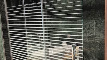 Een moderne badkamer met een douchecabine van glas, marmeren tegels en een houten bankje.