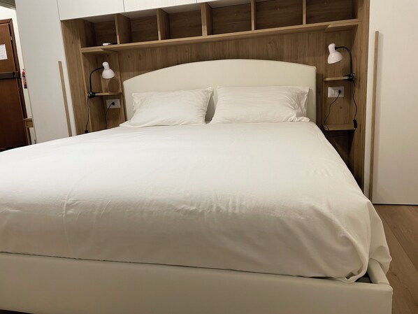 A neatly made bed with white bedding, wooden headboard, and two bedside lamps. - Silvia's House: cozy and comfortable. A 20-minute walk from Lake Como (Como)