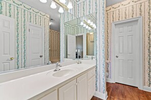 A bathroom with a large mirror, white vanity, and patterned wallpaper. - Gulf-Front Community Duplex across from the beach (Dauphin Island)