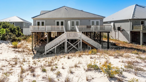 Une maison située en bord de mer, dotée d’une terrasse en bois et d’un escalier menant à un balcon.