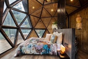 A room with a geometric wooden ceiling, a bed with floral bedding, a Buddha statue, and a view through large windows. - Green Oriental Resort (La Vega)