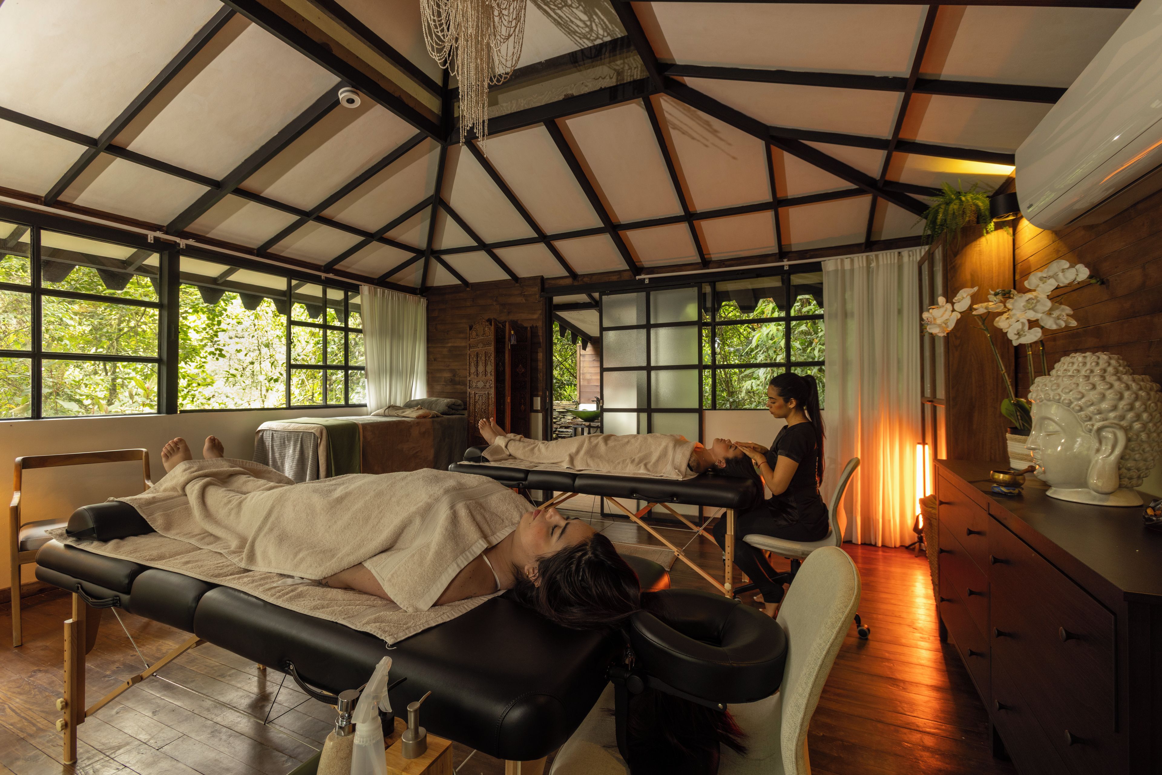 A spa room with two massage tables, a wooden ceiling, and large windows.