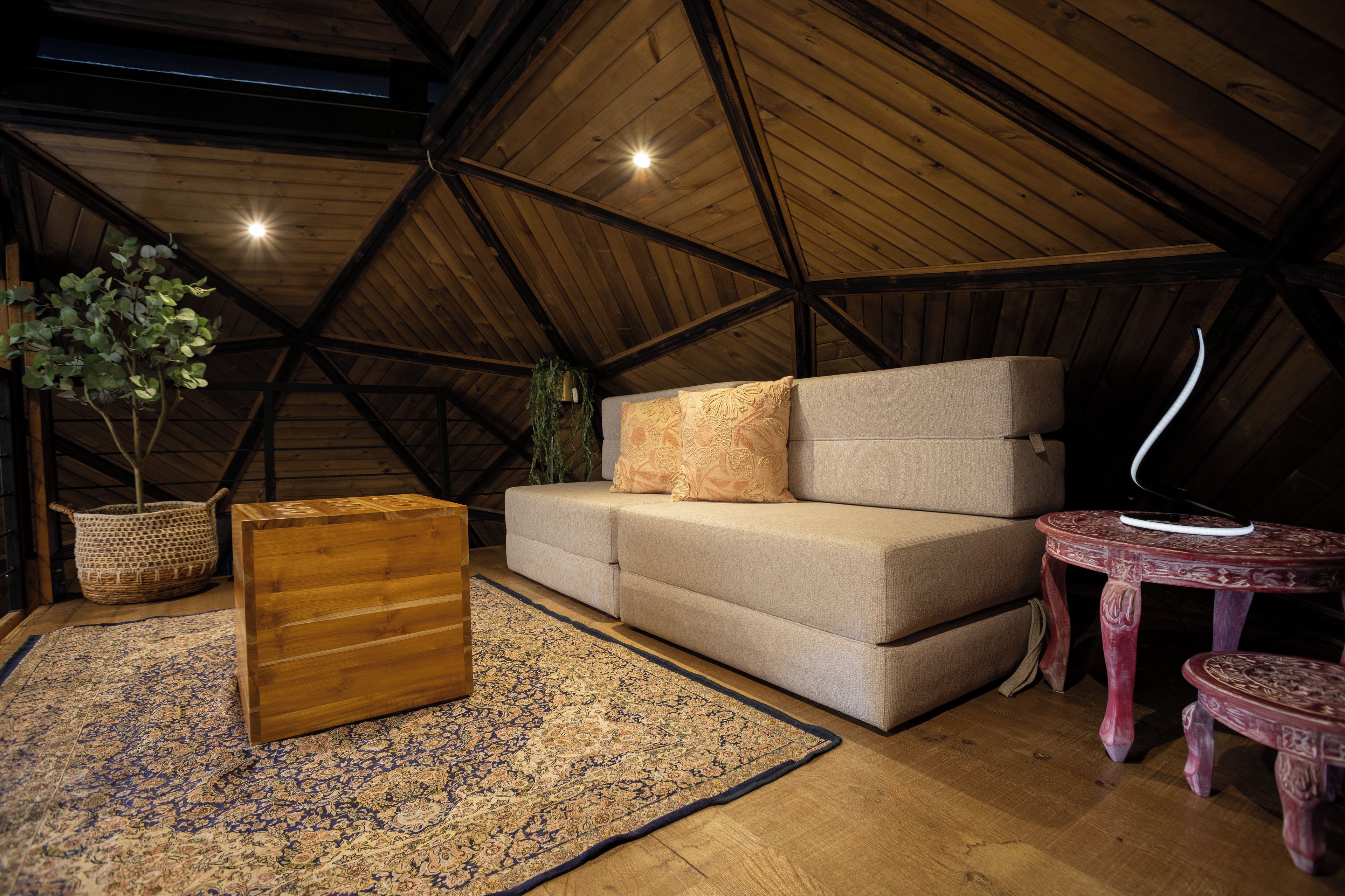Quarto de loft acolhedor com teto de madeira, sofá, mesa pequena e tapete decorativo.