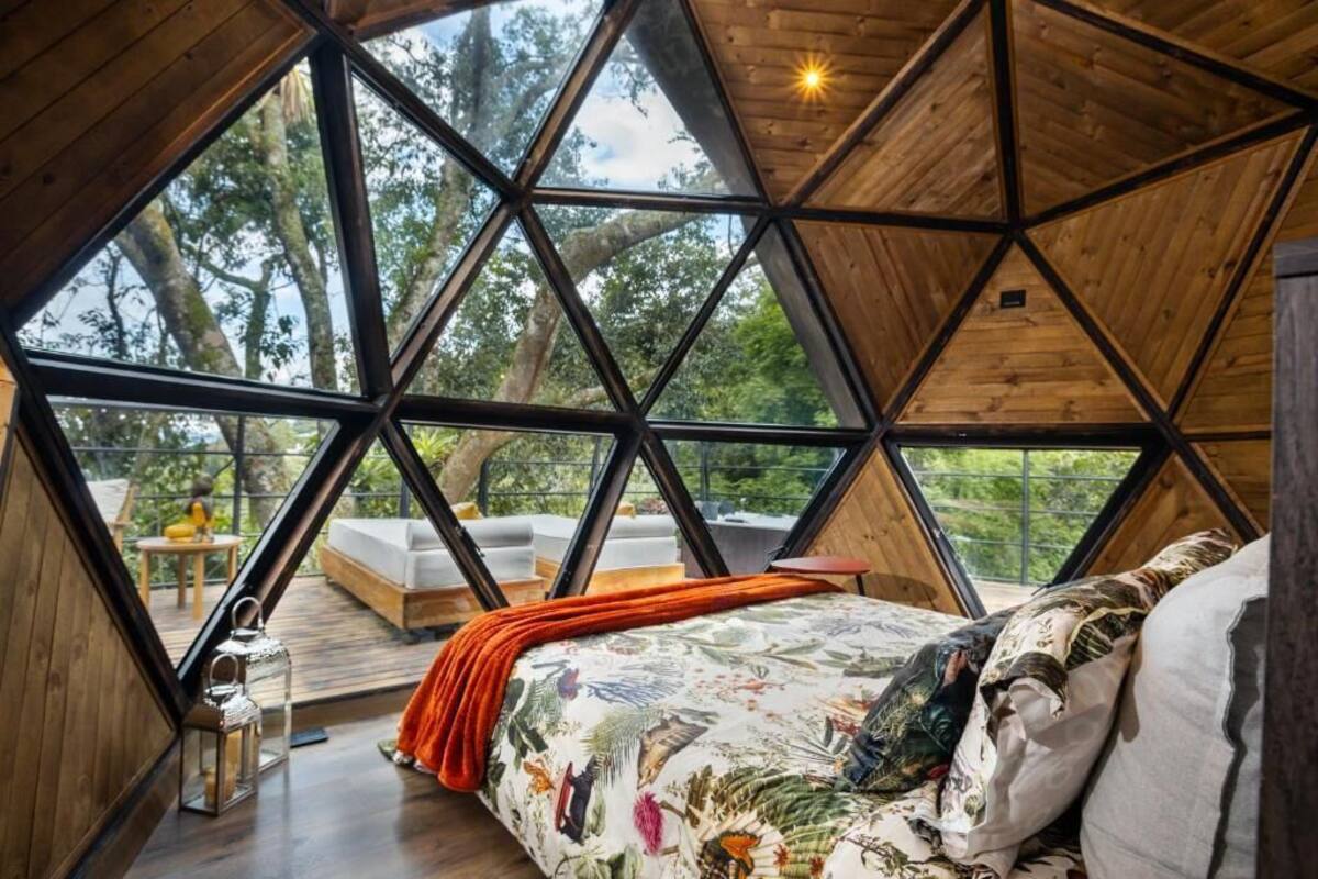 A geometric wooden room with a bed, a small table, and a view of the outdoors.