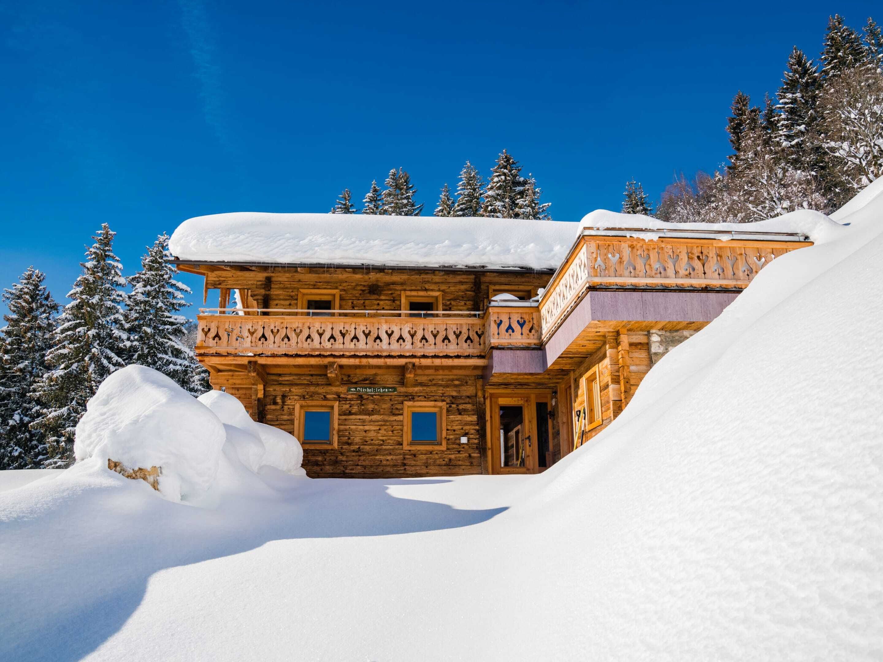 A wooden chalet with a balcony, surrounded by snow-covered trees.