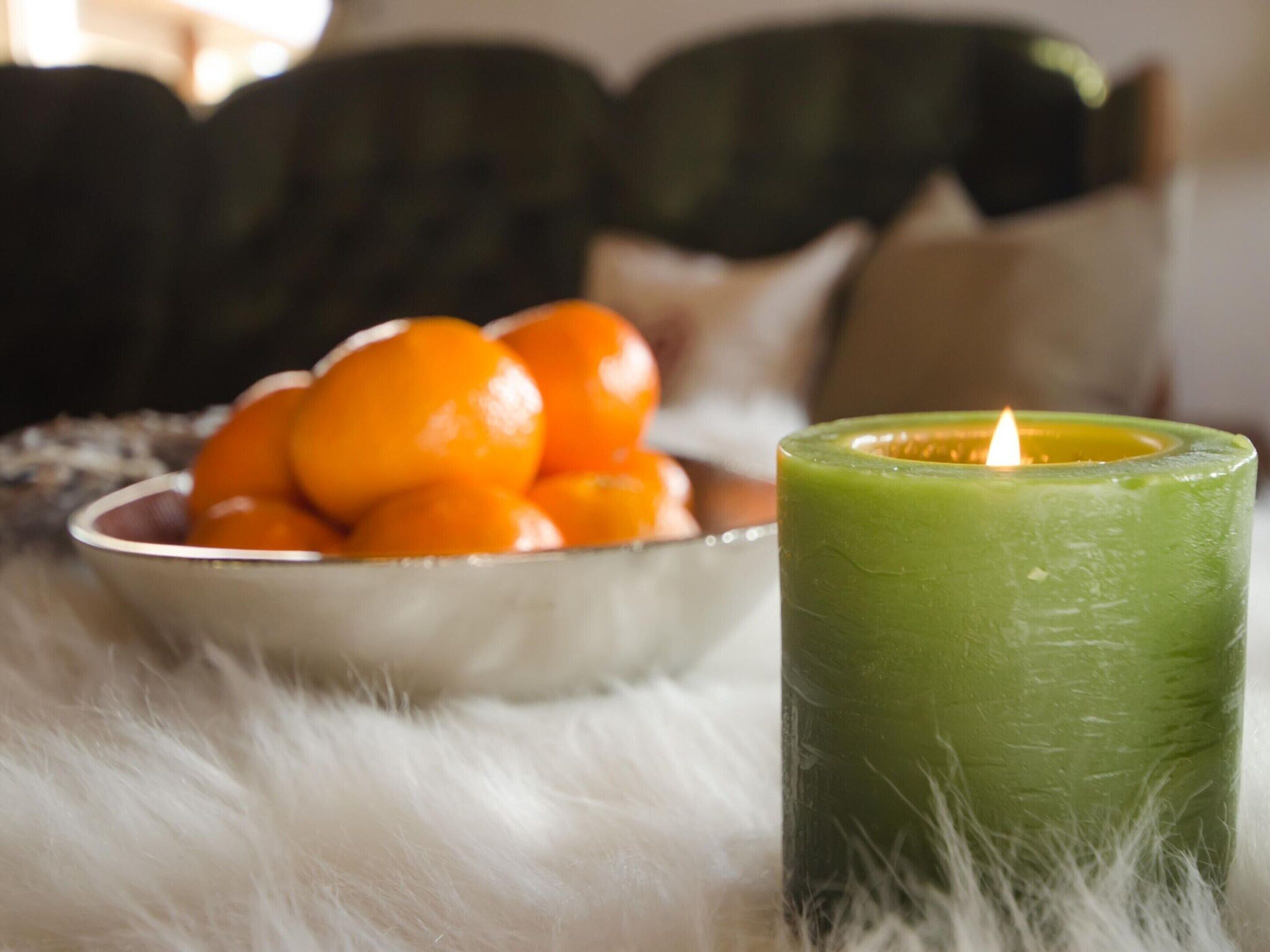 A bowl of orange fruit and a green candle on a fluffy surface.