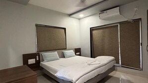A modern bedroom with a bed, nightstands, a wooden dresser, a ceiling fan, and an air conditioning unit. - Encasa Resort  (Alibag)