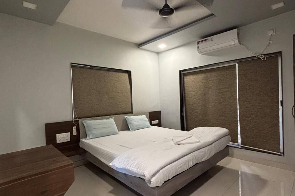 A modern bedroom with a bed, nightstands, a wooden dresser, a ceiling fan, and an air conditioning unit.