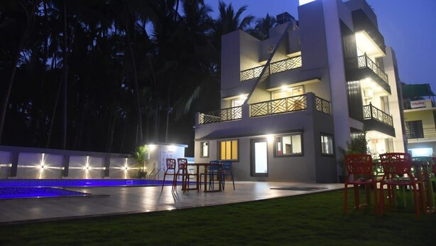 A modern hotel with a two-story structure, outdoor seating area, and a visible sign indicating the name. - Encasa Resort  (Alibag)