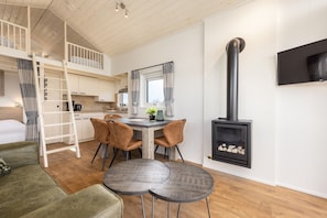 A loft-style room with a dining area, a loft bed, a fireplace, and a TV mounted on the wall.