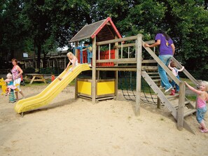 Une aire de jeux avec un toboggan, des structures d’escalade et un petit bâtiment.