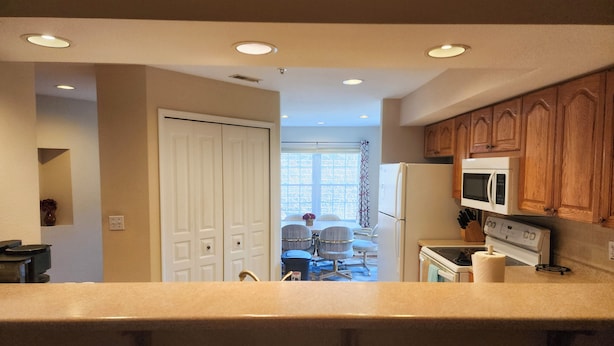 A kitchen with wooden cabinets, a refrigerator, a microwave, and a dining area with a table and chairs. - Golf View Condo | 2 King Suites + Sunroom | Sleeps Groups Comfortably | FW 7-1 (Branson)