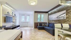 A modern living room with a sofa, a dining table, a TV, and a fireplace. - Imperial Apartments - Seaside (Sopot)