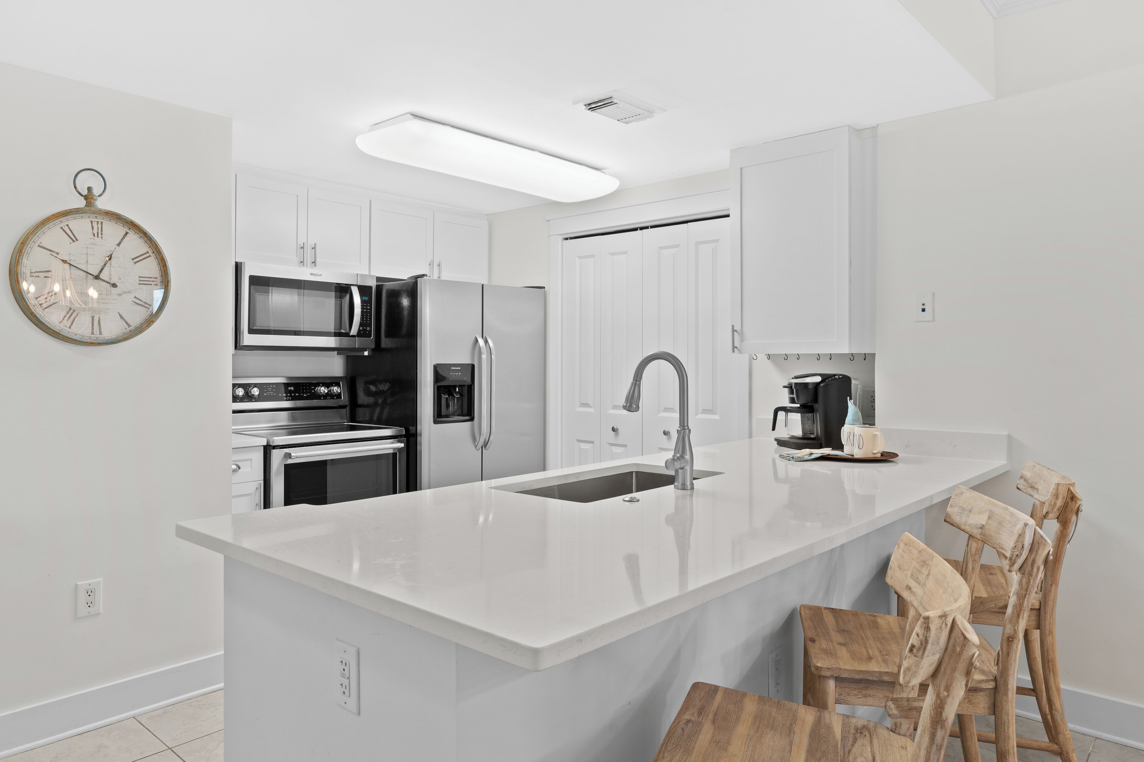 A modern kitchen with white cabinetry, stainless steel appliances, a central island with a sink, and a wooden chair.