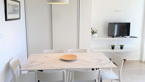 A modern dining area with a marble table, white chairs, a pendant light, and a TV on a shelf.