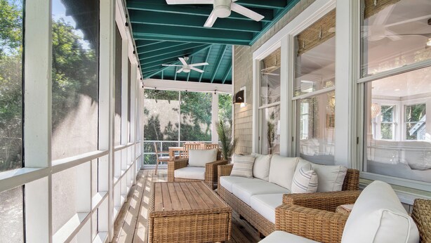 A covered porch with wicker furniture, ceiling fans, and large windows. - 3 bedroom home by golf course with maritime forest views (Bald Head Island)