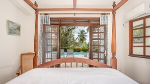 A bedroom with a wooden canopy bed, a view of an outdoor swimming pool, and a wicker chair. - Villa with beautiful pool tropical garden 6 p (Rivière-Salée)