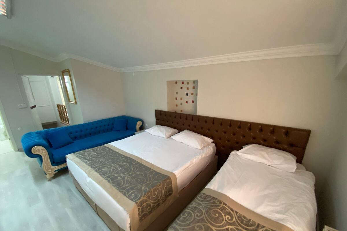 Habitación de hotel con dos camas, un sofá azul y un panel decorativo en la pared.