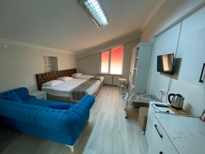 A hotel room with a bed, a blue sofa, a desk with a kettle, a TV, and a window with a view. - KUTLU SUİT'S (Ankara)