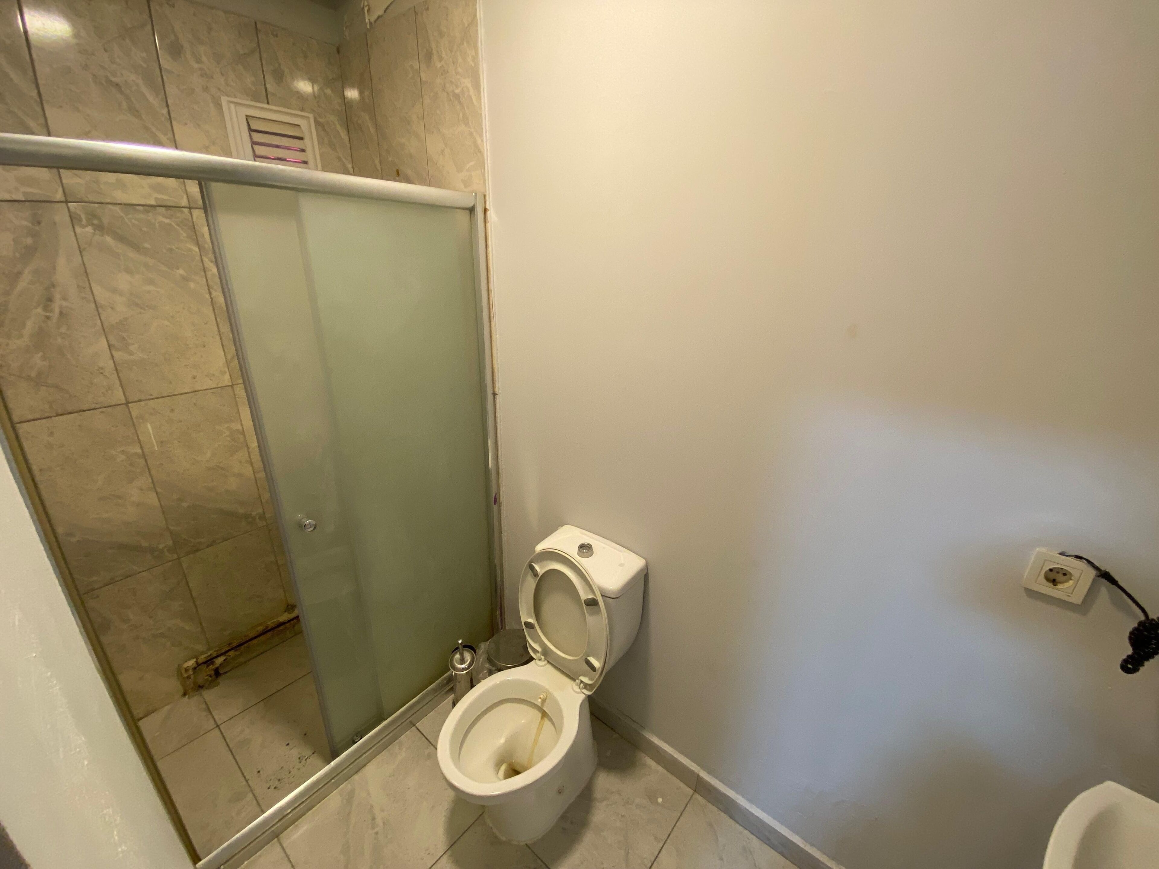 Ein Badezimmer mit Toilette, einer Duschkabine aus Glas und einer an der Wand montierten Steckdose.