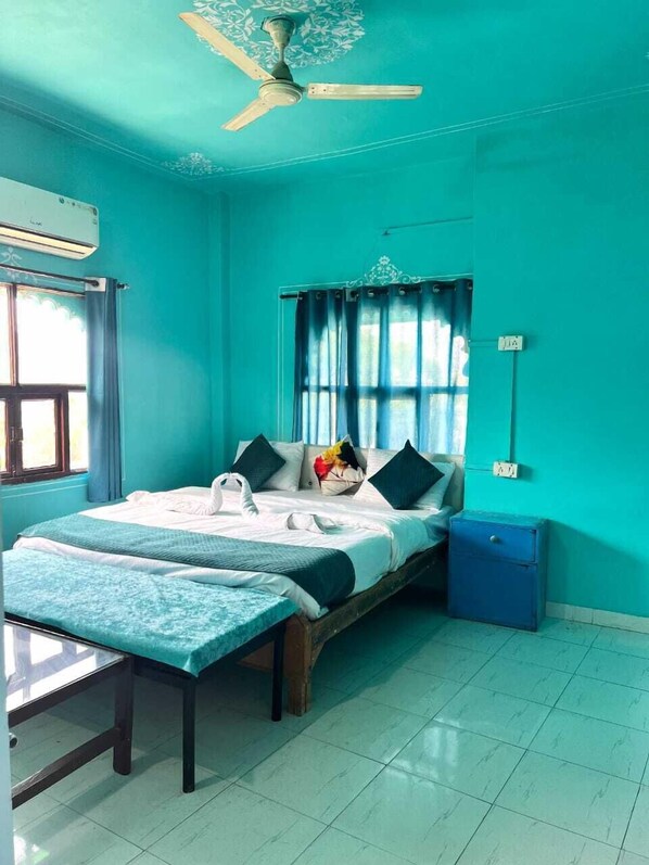 A room with a bed, a desk, a ceiling fan, a window with curtains, and a wall-mounted air conditioner. - The Hostel Crown (Udaipur)