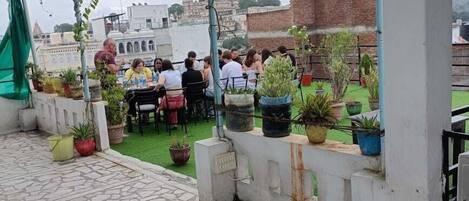 A rooftop patio with stone flooring, potted plants, and a group of people dining.