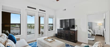 A spacious living room with a large TV, a ceiling fan, and a view of the outdoors through the sliding doors.