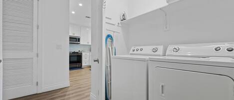 A laundry room with two washing machines and a dryer, a microwave, and a small kitchen area with cabinets and a countertop.
