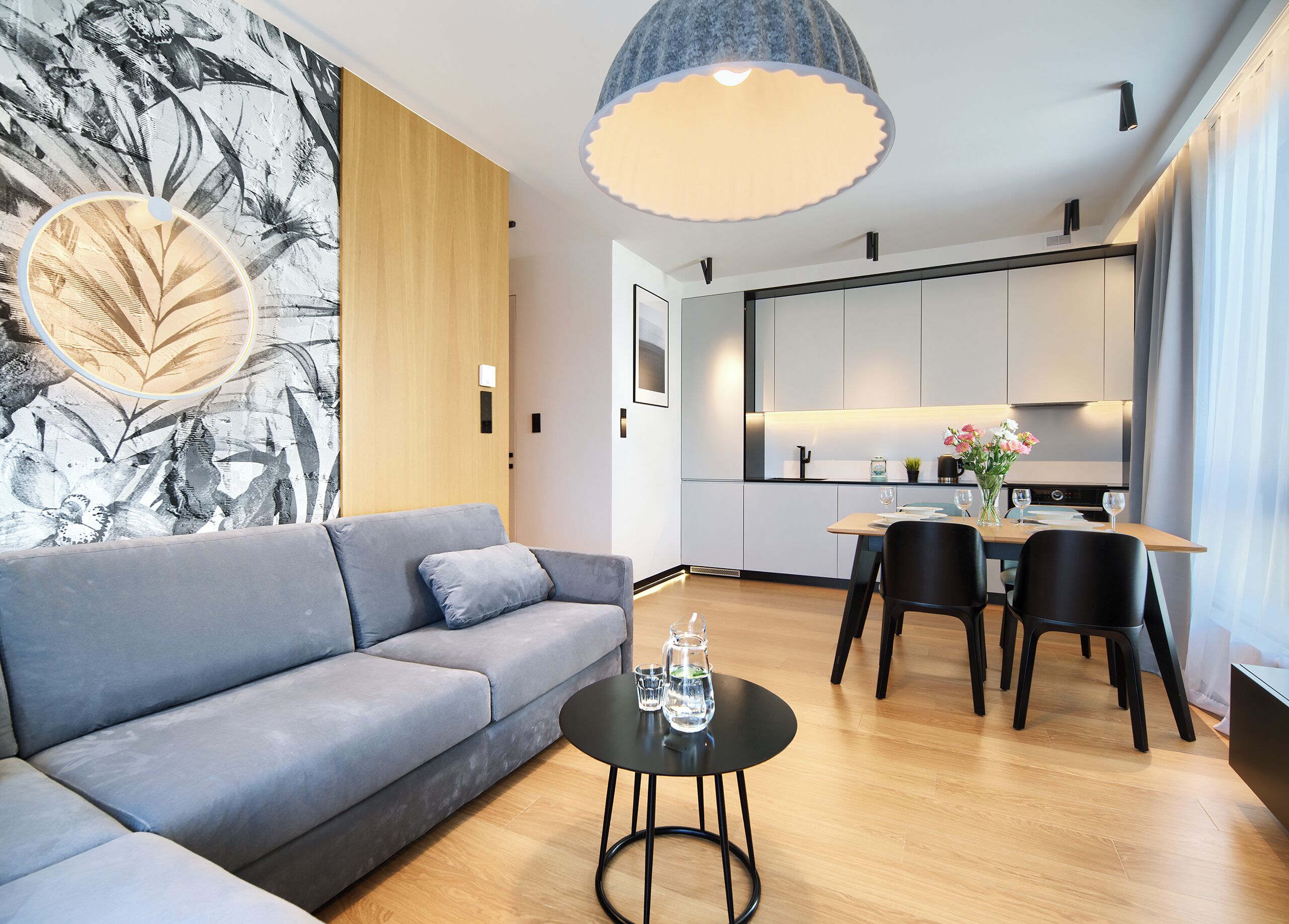 Una sala de estar moderna con un sofá gris, una mesa de centro negra redonda y un comedor con una mesa de madera y sillas negras.