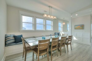 A dining area with a glass table, wooden chairs, a bench with cushions, and a painting on the wall.