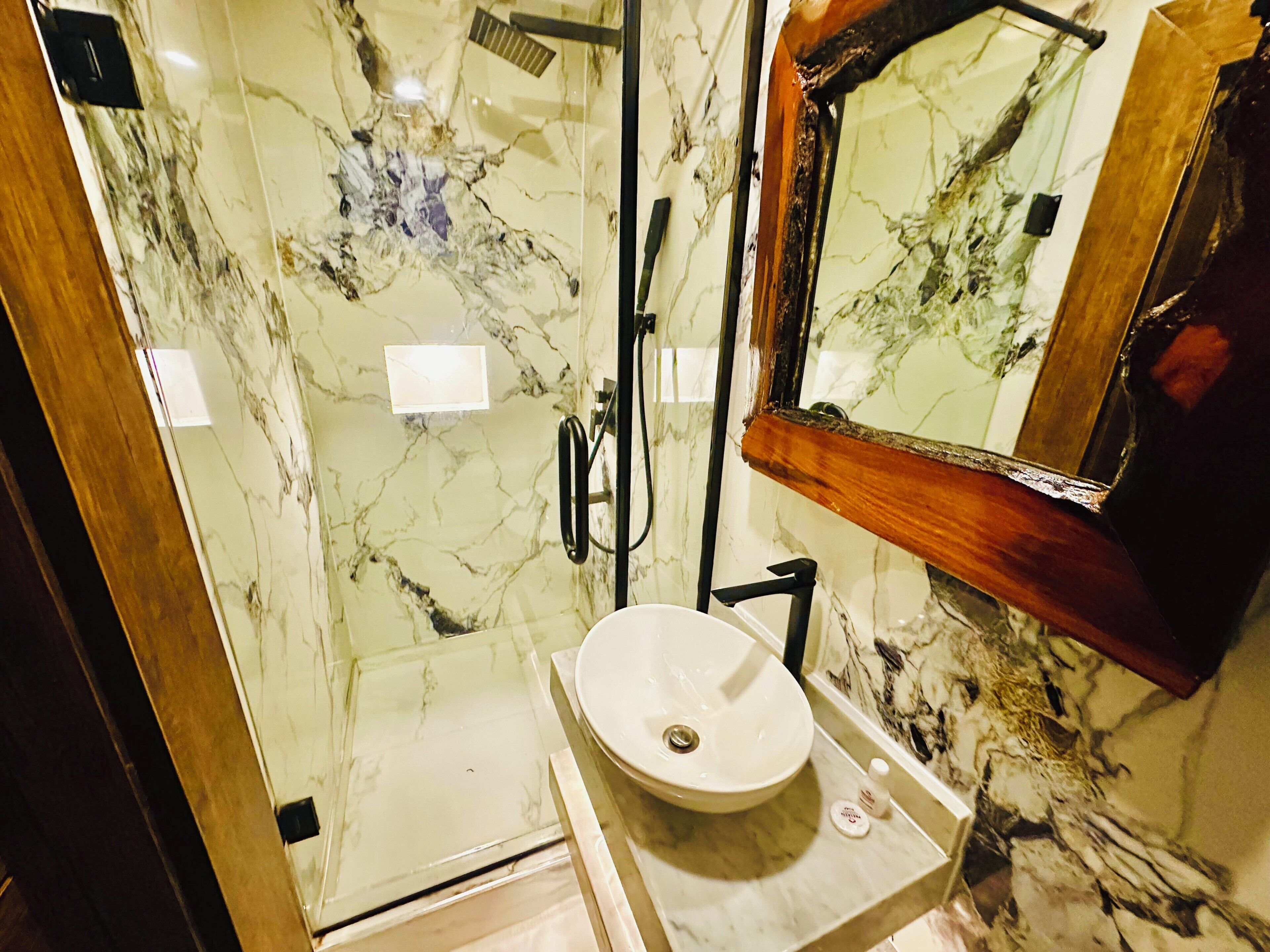 A bathroom with a marble wall, a sink, and a shower area.