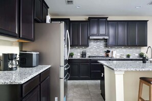 A modern kitchen with dark cabinets, granite countertops, a stainless steel refrigerator, and a built-in stove. - Arcade, Billiards with a non heated Pool Two master suites (San Antonio)